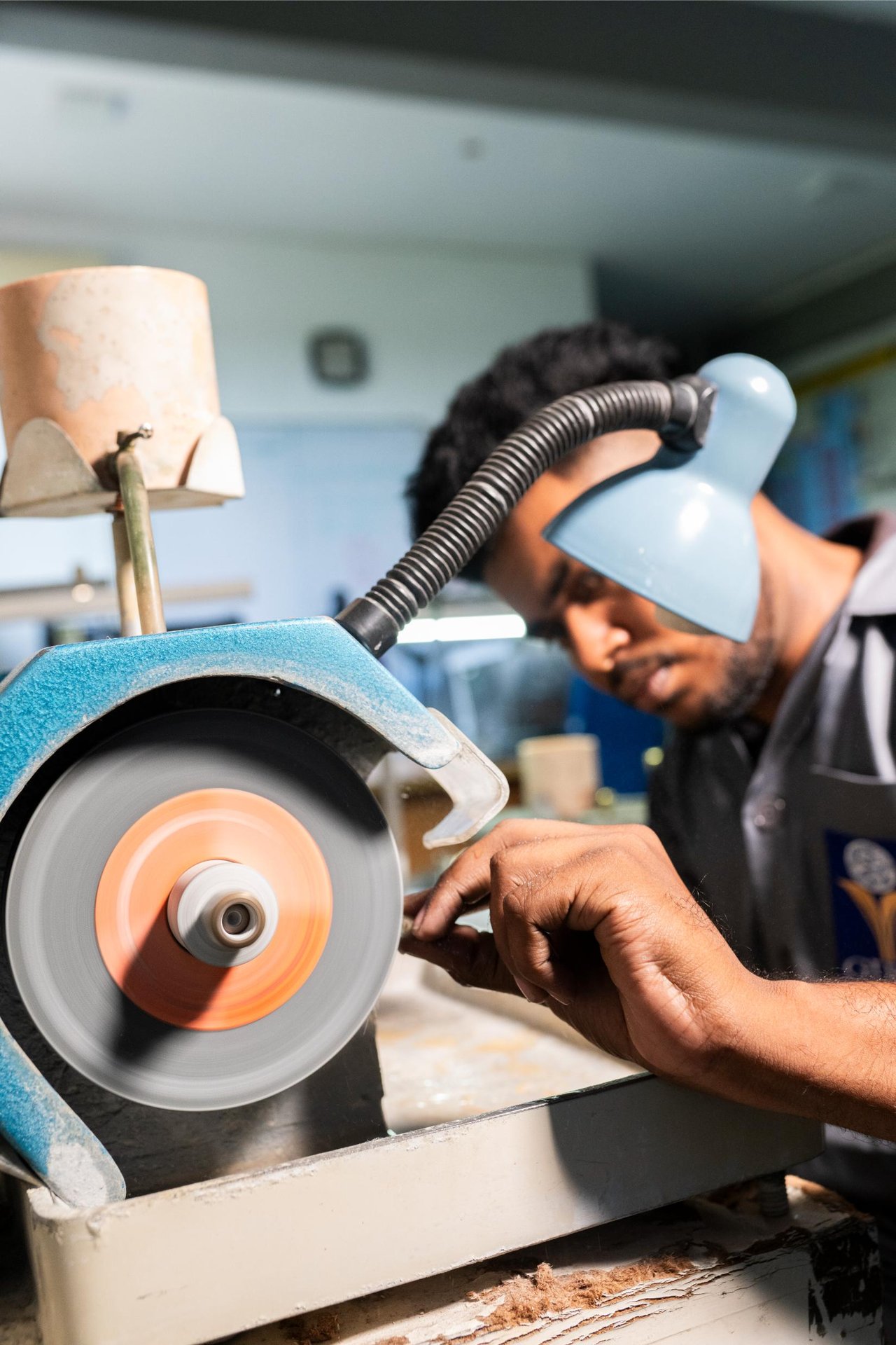 A gem cutter shaping a rough stone on a polishing wheel